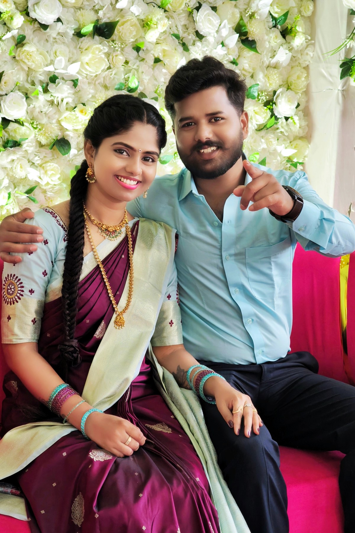 Naveen and Pavana seated together against a white flower wall
